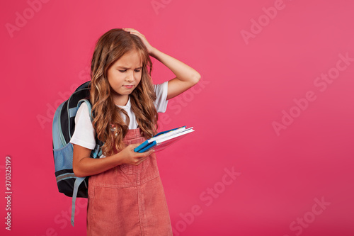 sad upset girl schoolgirl with books in her hands. photo on pink background