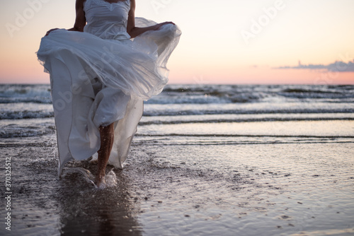 selective focus no face female running in the sunset sea waves in white dress