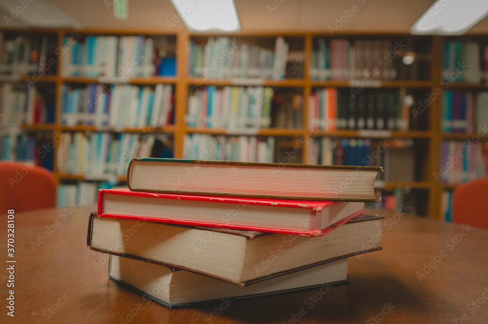 Stack of books on table and blurred bookshelf in the library room, education background. Stack of books on table and blurred bookshelf in the library room, education background.