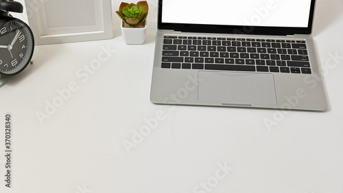 Close up of minimal workspace with laptop, clock, and frame on white table.