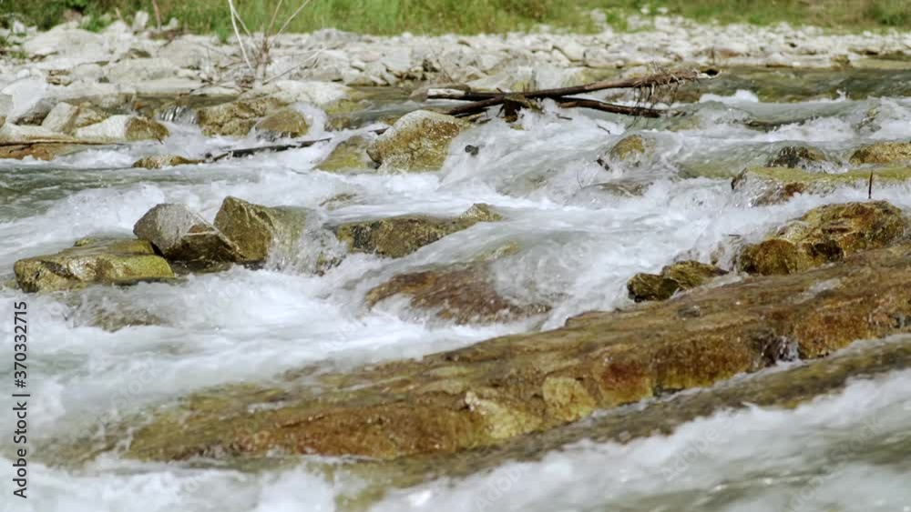 River flowing over rocks on sunny day, close up detail, rapid white water with blurred stones and grass background River flowing over rocks on sunny day, close up detail, rapid white water with blurred stones and grass background
