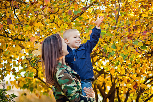 A young beautiful mother in warm clothes plays with her young son in the autumn Park.