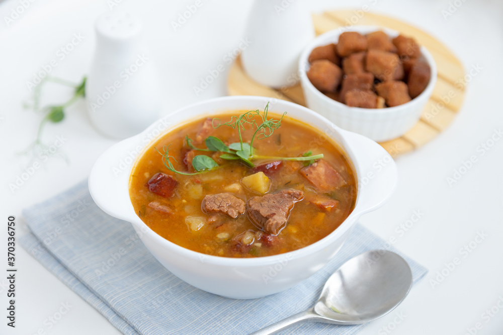 Pea soup with meat, smoked sausage, pea sprouts and croutons. Traditional Russian dish. Home kitchen. Close-up, selective focus. Pea soup with meat, smoked sausage, pea sprouts and croutons. Traditional Russian dish. Home kitchen. Close-up, selective focus.