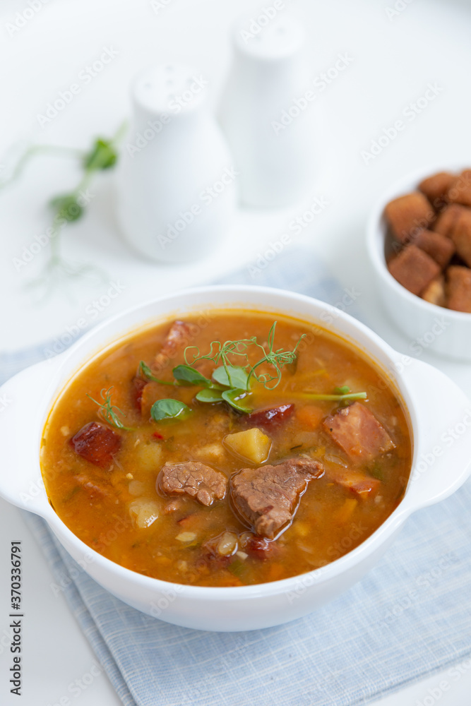 Pea soup with meat, smoked sausage, pea sprouts and croutons. Traditional Russian dish. Home kitchen. Close-up, selective focus. Pea soup with meat, smoked sausage, pea sprouts and croutons. Traditional Russian dish. Home kitchen. Close-up, selective focus.