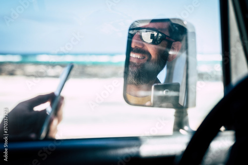 close up of young man smiling and having fun using his phone or device driving his car at the beach with the sea or oceanand the sand at the background - happy people discovering with car vehicle © simona