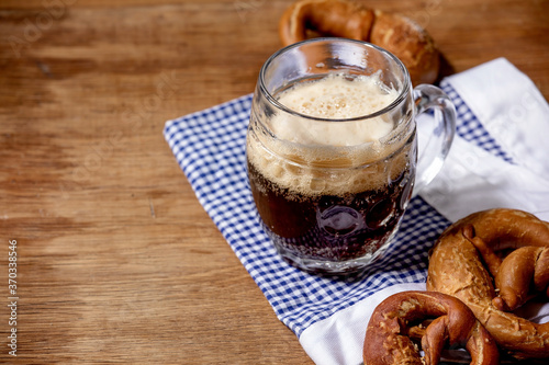 Glass of lager beer with traditional salted pretzels on white and blue napkin over wooden background. Oktoberfest theme