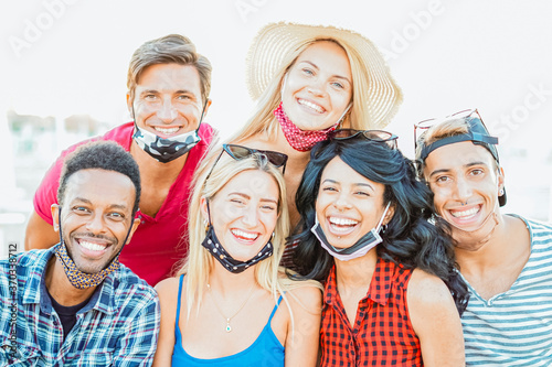 Group of multiracial friends taking a picture while focusing the camera and smiling with face mask - New lifestyle concept