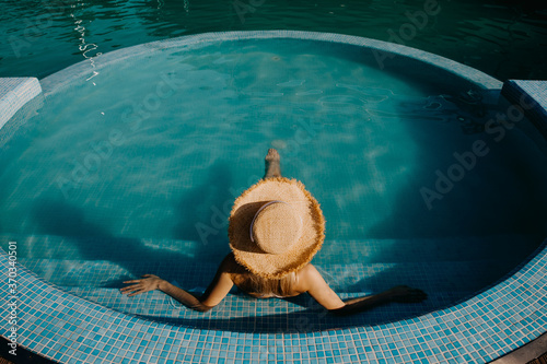 Top view over a young woman sitting in a pool, wearing a straw hat.
