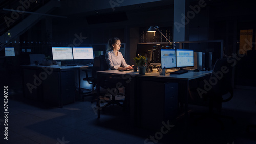 Working Late at Night in the Office: Businesswoman Uses Desktop Computer, Analyzing, Using Documents, Solving Problems, Finishing Important Project. Diligent Ambitious Young Worker