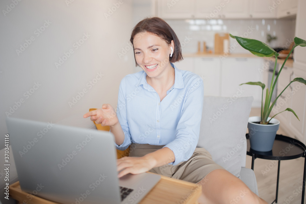 Work from home office, woman smiles and conducts business negotiations with employees via video call internet laptop, light background Work from home office, woman smiles and conducts business negotiations with employees via video call internet laptop, light background
