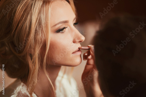 Make-up artist doing make up for young beautiful bride applying wedding make-up