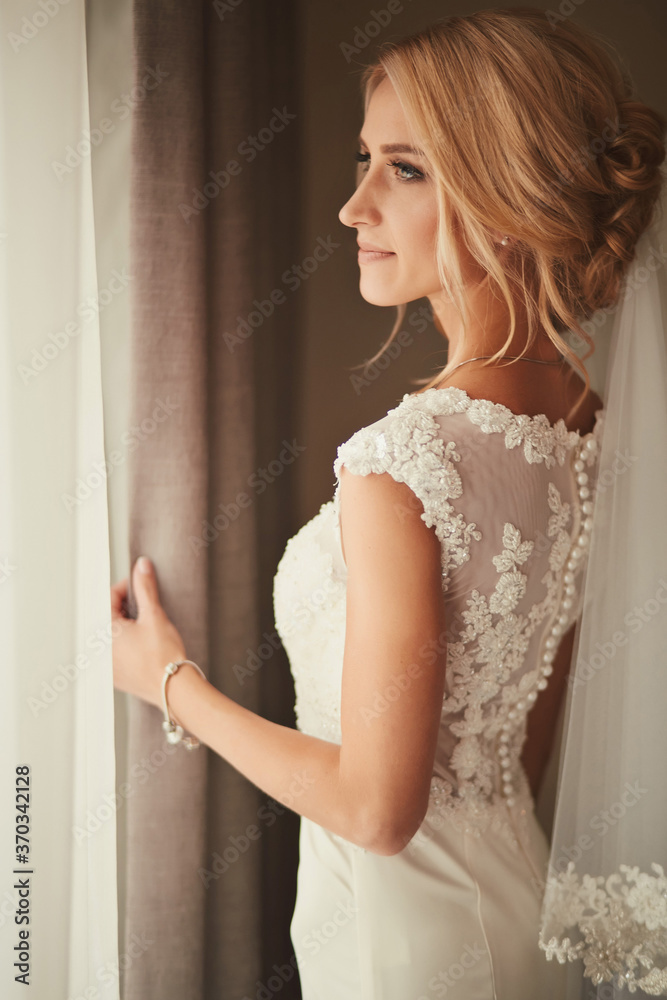 Beautiful bride standing near the window and smiling. Wedding Day