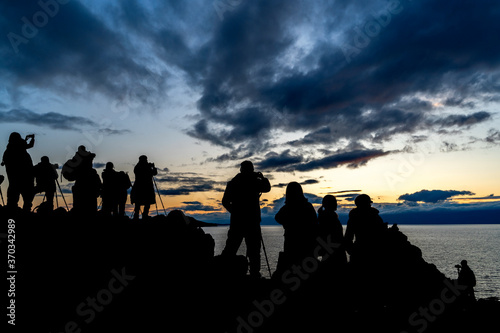 Faceless group of people on top of a mountain watching sunset, silhouette of group of people taking pictures outside during sunrise or sunset © Elena Sistaliuk