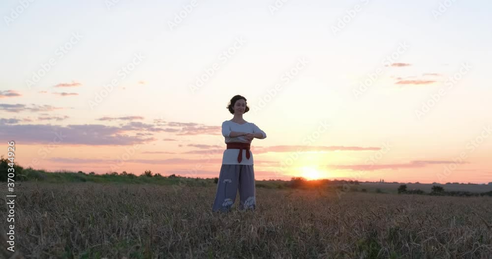 Female practicing qigong in summer fields with beautiful sunset on background Female practicing qigong in summer fields with beautiful sunset on background