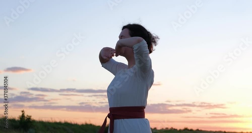 Female practicing qigong in summer fields with beautiful sunset on background 