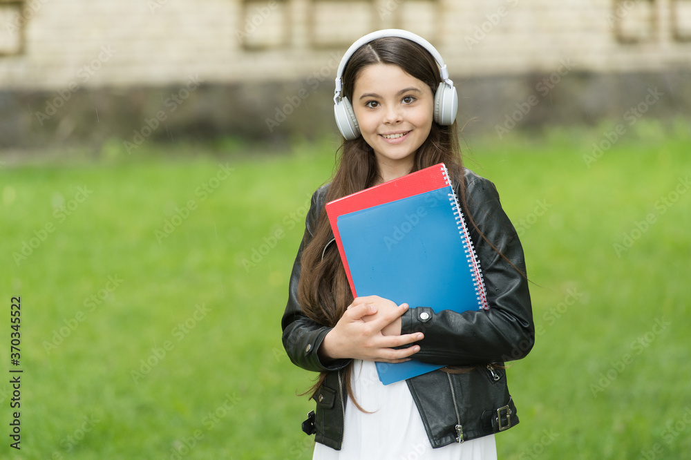 Fototapeta premium Girl listening audio carry textbooks on way to school, language lessons concept