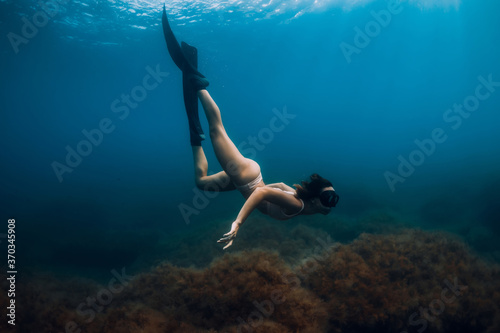 Sporty woman freediver with fins glides underwater in sea. Freediving in ocean