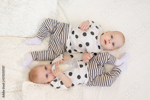 two baby twins brother and sister 8 months old lie on the bed in their pajamas and drink milk from a bottle, baby food concept, top view, concept of friendship, place for text