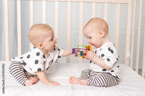 two twin babies 8 months old play in the crib, early development of children up to a year, the concept of the relationship of children of brother and sister, the child takes the toy from the other