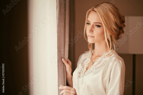 Beautiful bride standing near the window and smiling. Wedding Day