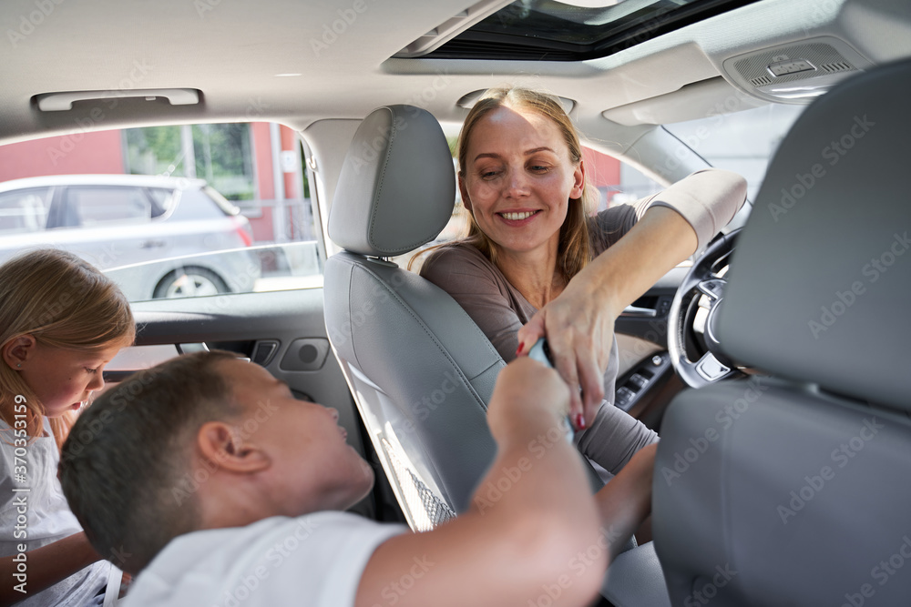 Happy woman giving smartphone to kids in car Happy woman giving smartphone to kids in car
