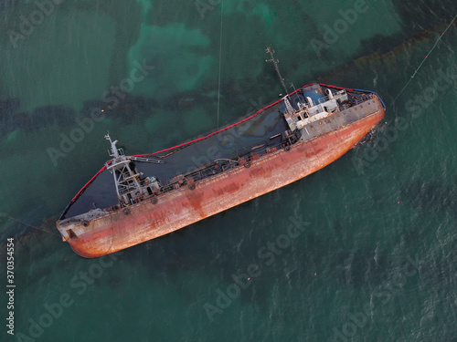 Top view of an old tanker that ran aground and overturned on the shore near the coast. A storm-swept old ship spilled oil and caused a major environmental disaster along the coast. photo