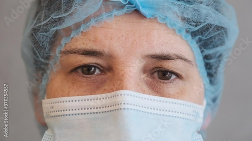 sad and tired medic opens eyes and looking atraight at camera. medical stuff portrait closeup. Woman in Protective Face Mask photo