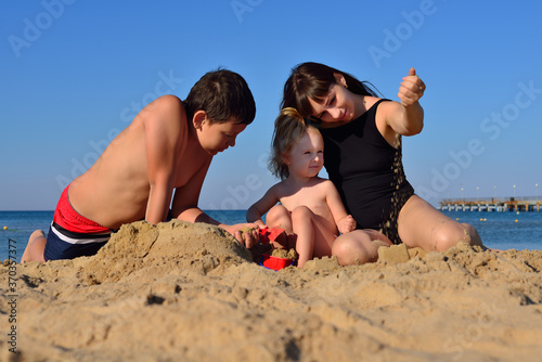Mom, son and daughter are playing in the sand on the beach