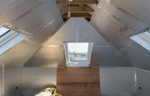 Loft conversion, unfinished project, silver insulation, roof windows wood structure, selective focus photo