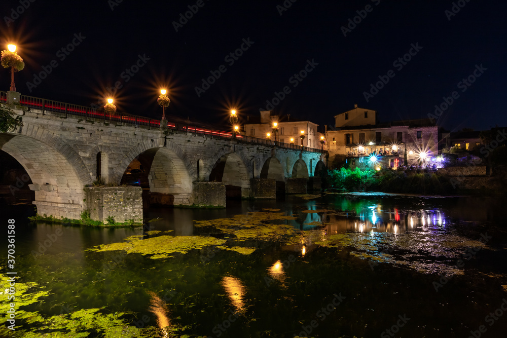 Vue nocturne sur le Pont Tibère et sa réflexion sur les eaux du fleuve Vidourle à Sommières (Occitanie, France)