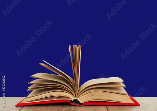 Open book textbook in a red cover on a wooden desk with blue background. Back to school distance home education.Quarantine concept of stay home.