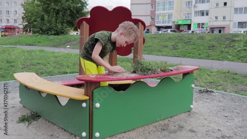A preschool boy plays in a sandbox on a playground in the courtyard of a house, video