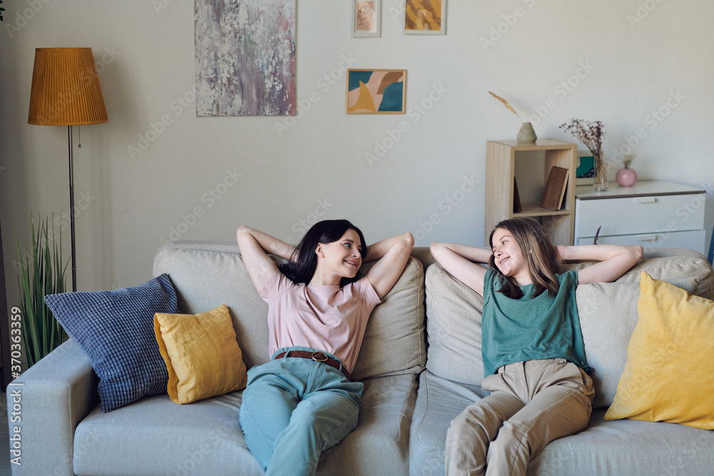 Obraz premium Cheerful and relaxed mother and daughter in casualwear chatting on couch