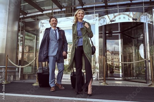 Cheerful woman and a happy man leaving a hotel with their luggage