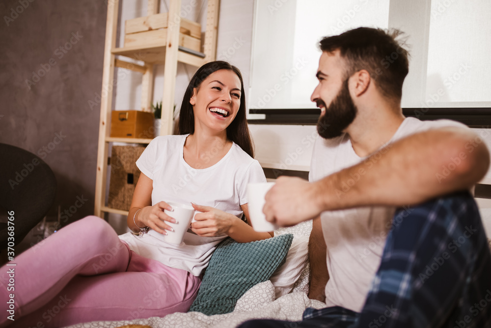 Smiling young couple in bed drinking coffee and looking each other. Smiling young couple in bed drinking coffee and looking each other.