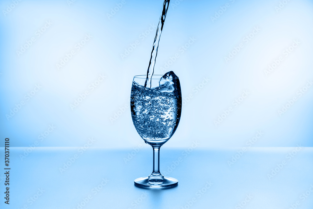 Pouring water into glass on blue background Pouring water into glass on blue background