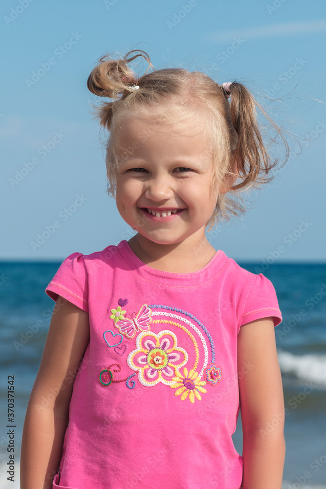 Little blonde girl in a pink T-shirt stands on a background of the sea. holidays with children near the ocean Little blonde girl in a pink T-shirt stands on a background of the sea. holidays with children near the ocean