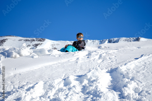 Young Boy Sitting On The Snow Mountain. Winter time