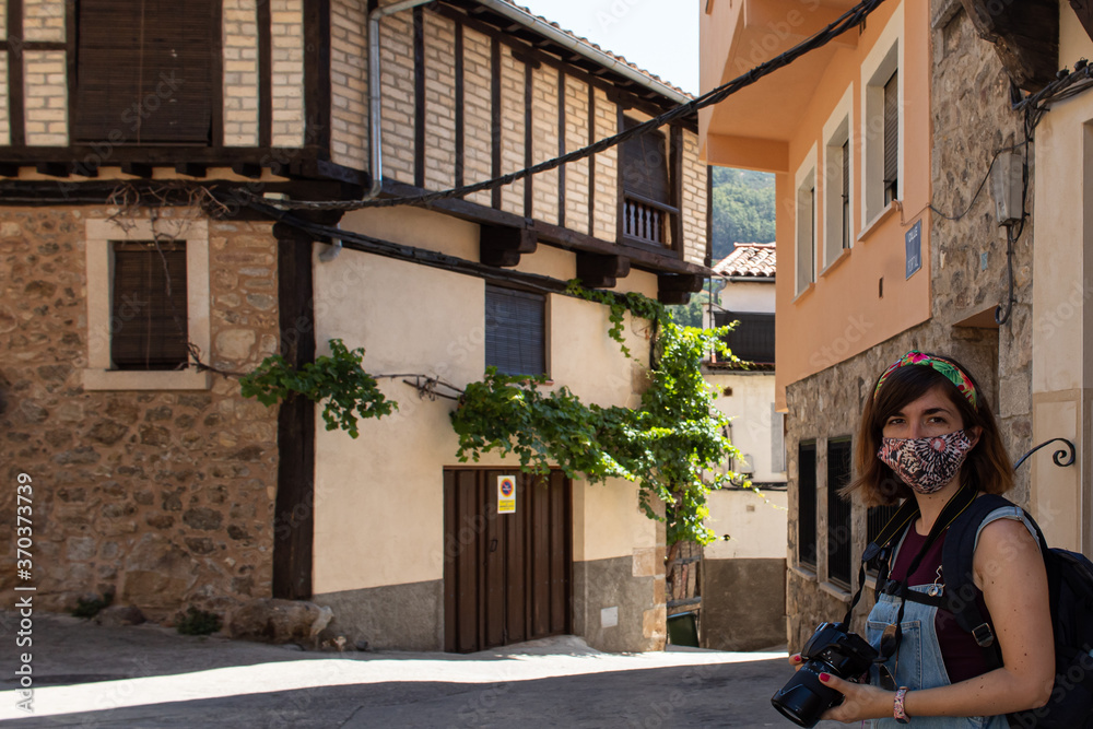 Attractive young female visiting an old town in Extremadura, Spain with a face mask and taking photos with a reflex camera