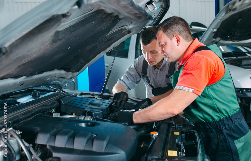 Two handsome mechanics in uniform are working in auto service. Car repair and maintenance. Two handsome mechanics in uniform are working in auto service. Car repair and maintenance.