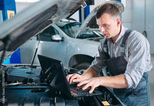 car mechanic using a computer laptop to diagnosing and checking up on car engines parts for fixing and repair.