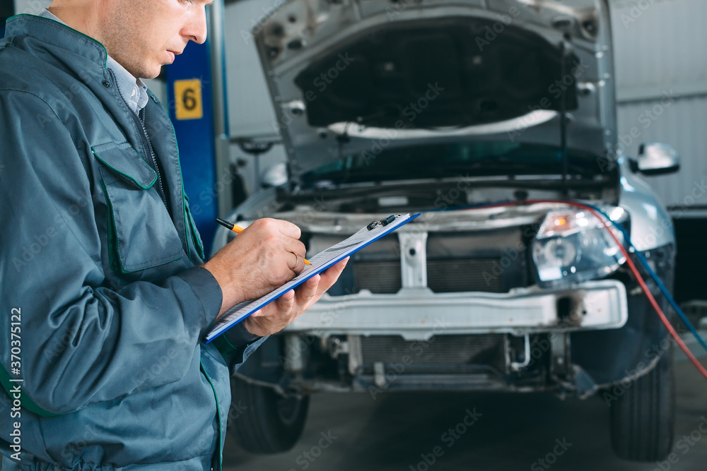 mechanic maintaining car record on clipboard at the repair shop. mechanic maintaining car record on clipboard at the repair shop.
