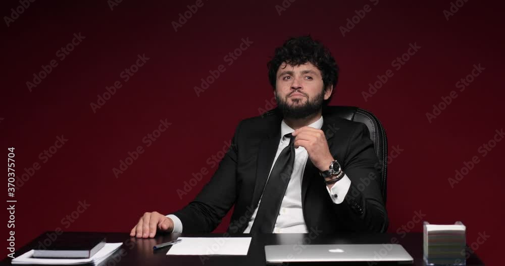 Young businessman sitting at his table thinking and writing his ideas on a sheet of paper then crumbling it, isolated on red background. Young businessman sitting at his table thinking and writing his ideas on a sheet of paper then crumbling it, isolated on red background.
