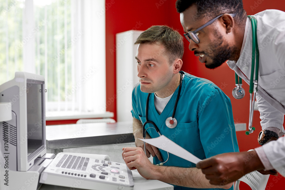 caucasian vet doctor and black assistant discuss pet pathology using special monitor equipment in clinic, conduct medical examining of animal