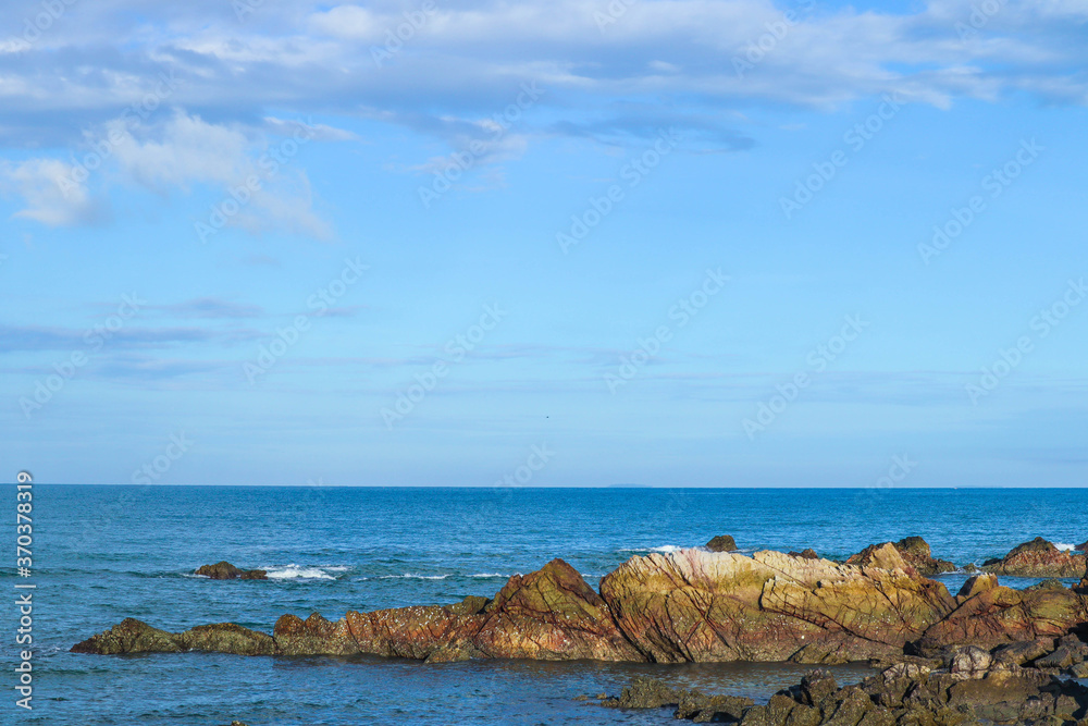 Seascape with rocks and splashing water in a windy summer day and blue sky.