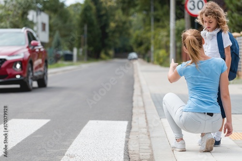 Fototapeta Naklejka Na Ścianę i Meble -  Young mother squats on the sidewalk and explains to the little boy how to cross the street safely