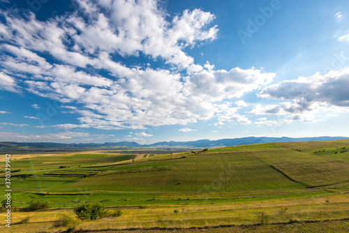 Beautiful blue sky with white clouds over green agricultural fields at summertime, visible lens flare.