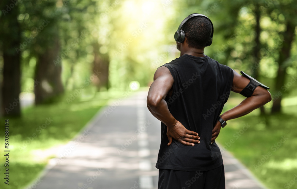 African guy sportsman rubbing his back, exercising at park African guy sportsman rubbing his back, exercising at park