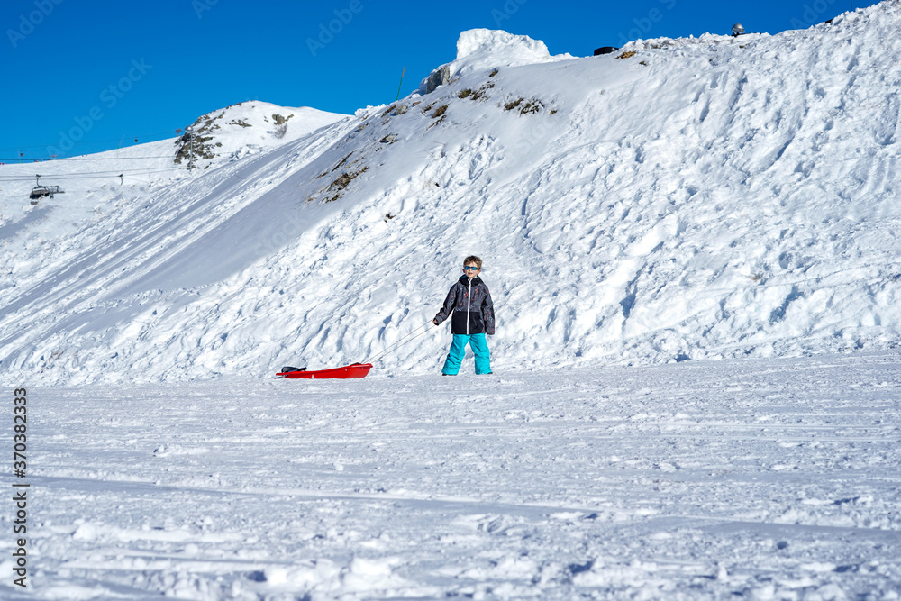 Boy with red sled in snow. Snow mountain background. Winter holidays 