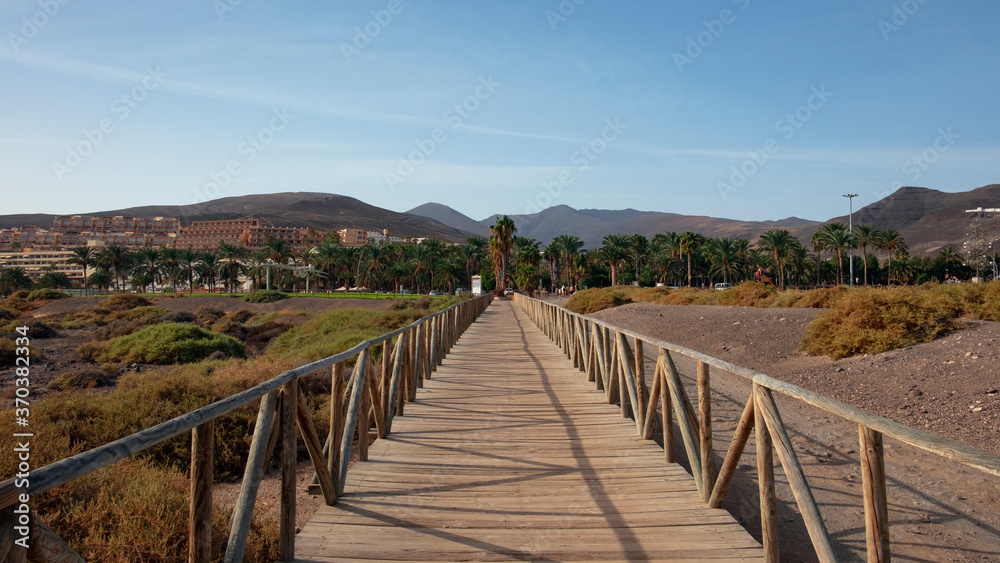 Wooden boardwalk connecting Jandia salt marsh, an unusual protected natural habitat and Morro Jable lighthouse to the coquette resort in the south of the island of Fuerteventura, Canary Islands, Spain
